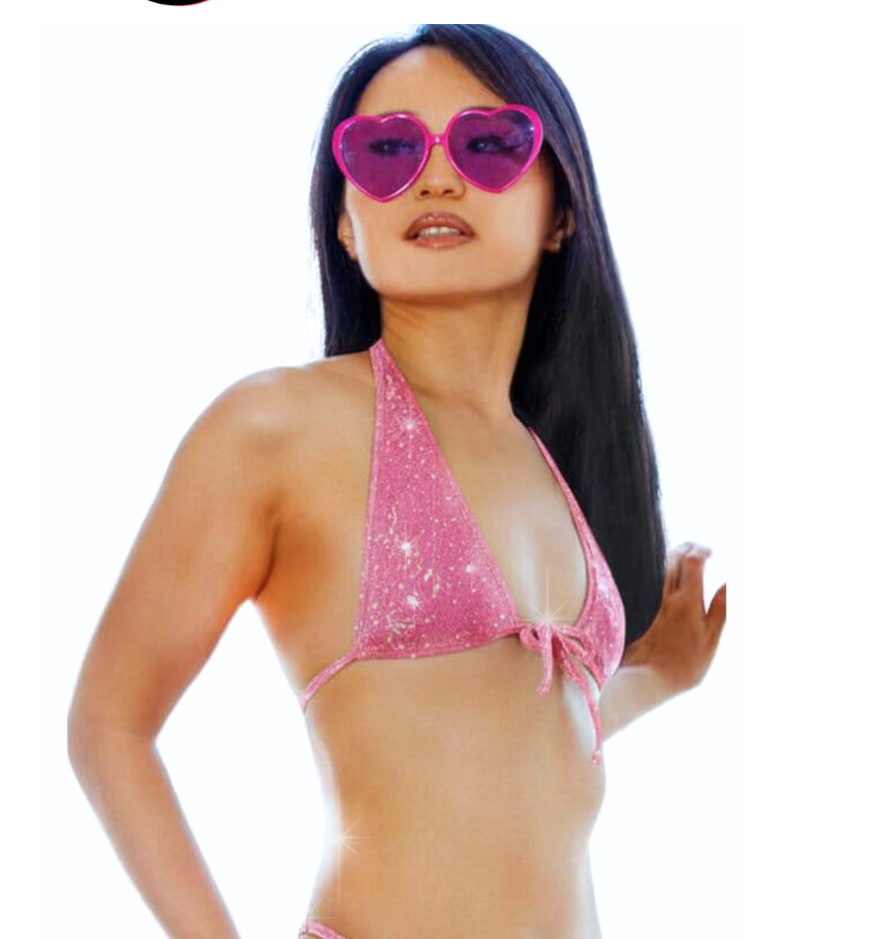 A model wearing a pink hologram tie halter crop top covered with shiny rhinestones and she is wearing matching colored sunglasses in the shape of a heart.
