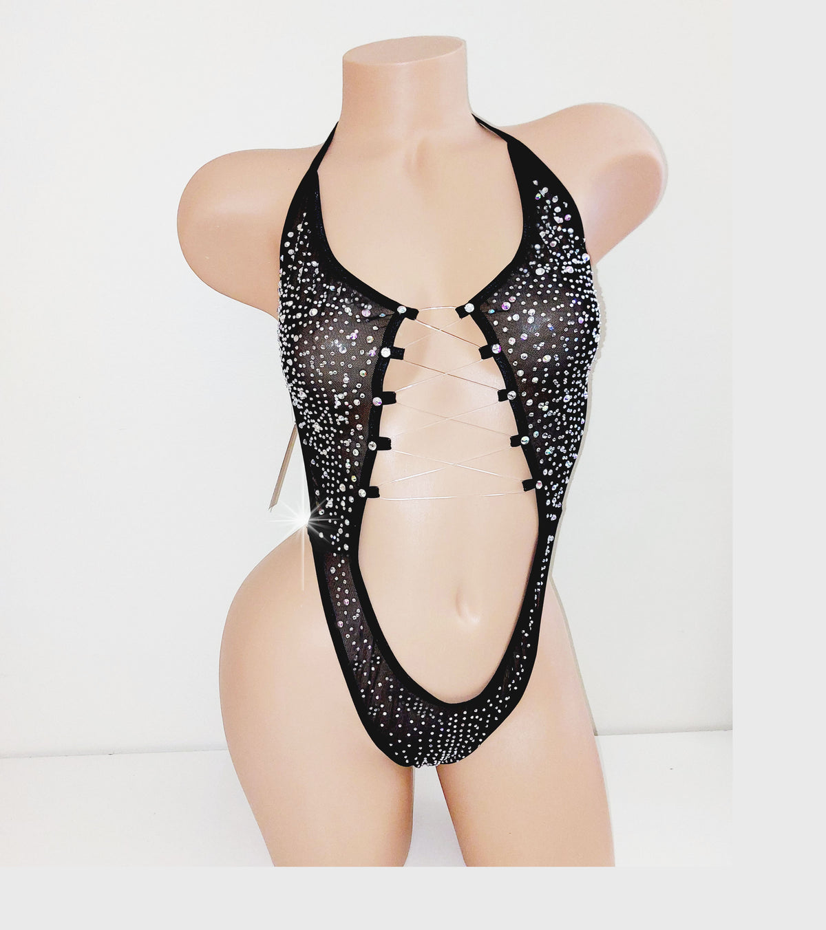 Black mesh one piece covered in rhinestones on a beige plastic mannequin torso against a plain background. 
