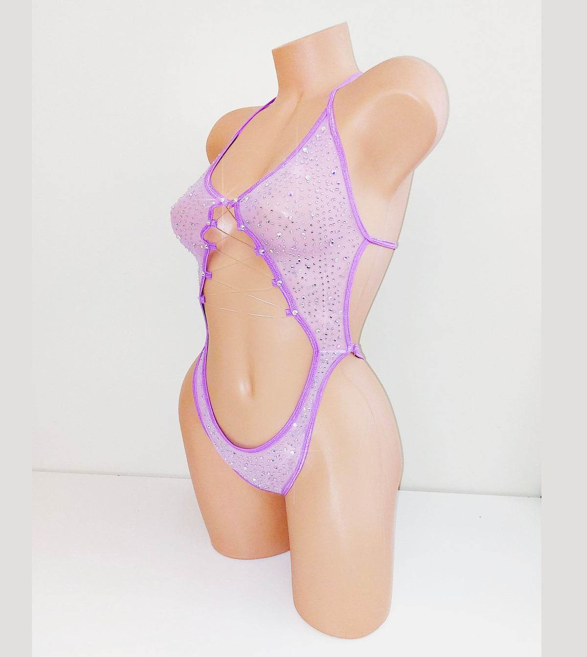 Lavender purple mesh one piece bodysuit leotard on a plastic beige mannequin, coveed in multi-sized rhinestones, against a blank background.