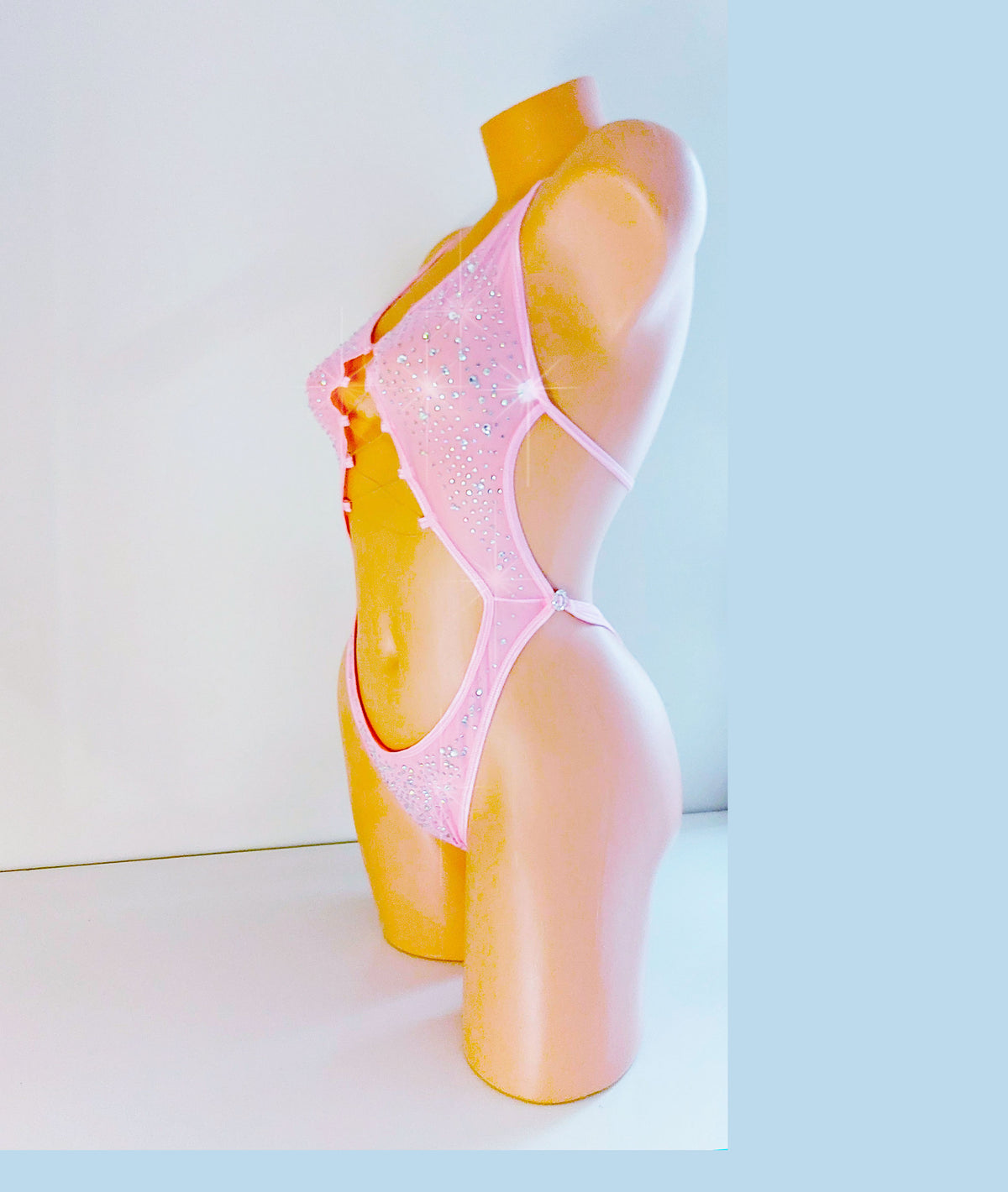 One-piece baby pink leotard bodysuit on a plastic beige mannequin torso, coveered in sparkling rhinestones all over.