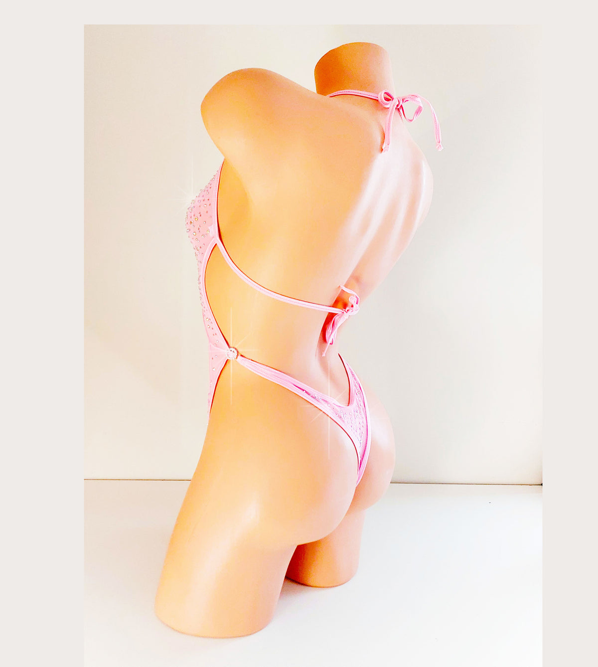 Side and back view of a One-piece baby pink leotard bodysuit on a plastic beige mannequin torso, coveered in sparkling rhinestones all over.