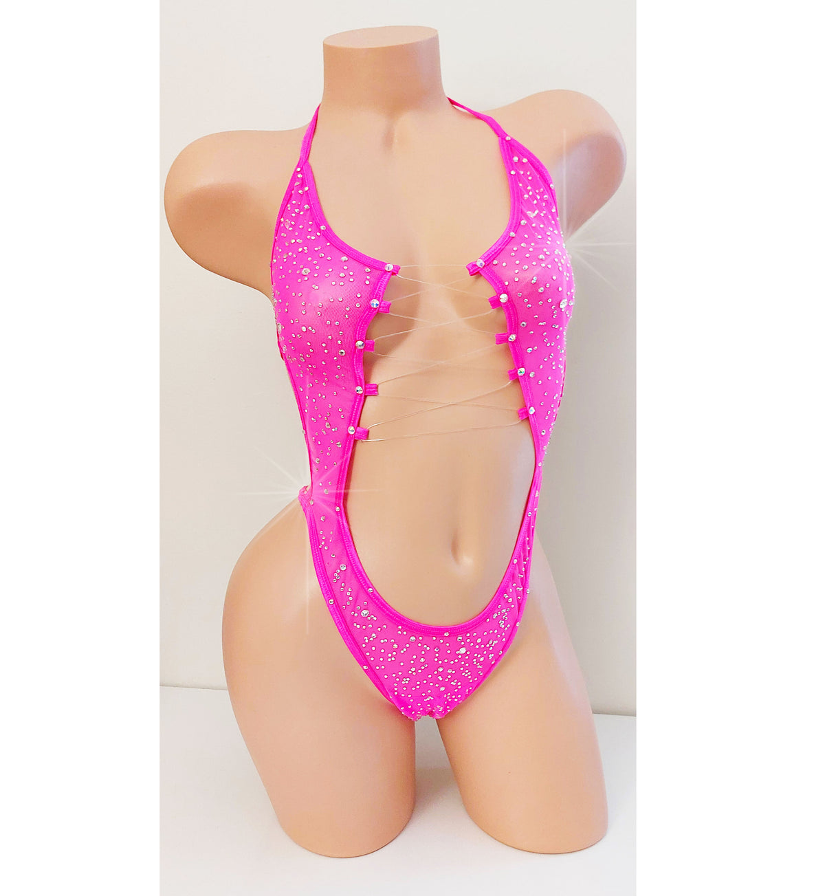 A beige mannequin displaying a bright hot pink colored one piece bodysuit leotard with a tummy cutout and totally covered in sparkling rhinestones.
