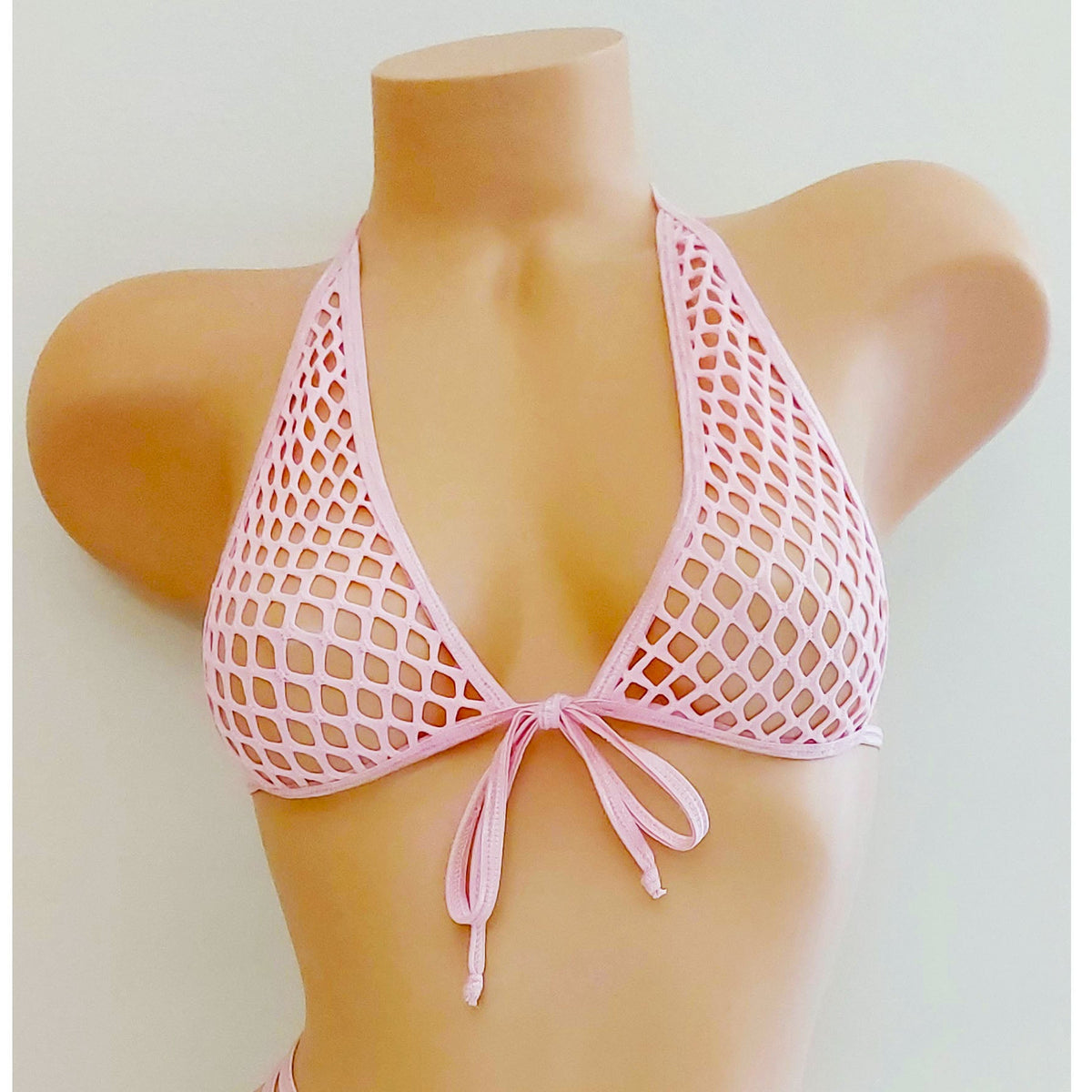 A two-piece pink fishnet bikini set displayed on a tan mannequin torso against a plain light background. The set includes a halter-style triangle top with a front tie and matching strappy low-rise bottoms.