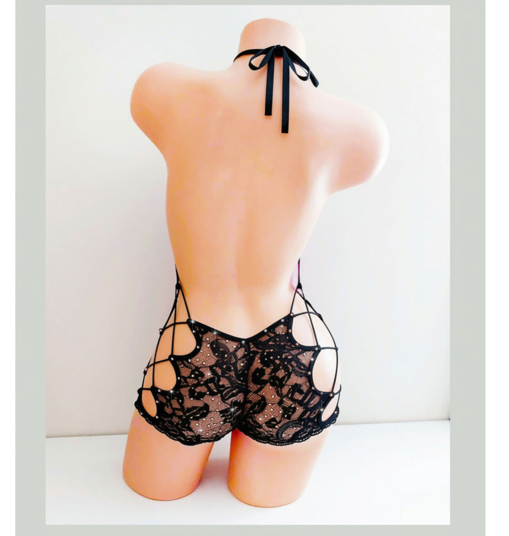 Back view of a Beige mannequin torso displaying a black lace shorts one piece with side cutouts and lace ups, with rhinestone accents. 