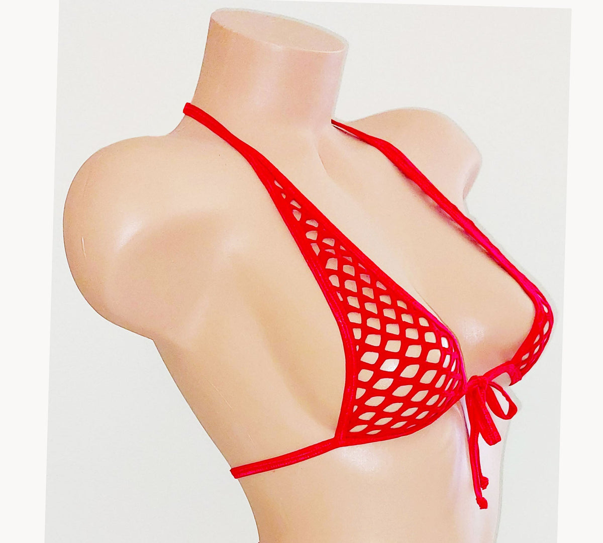 side view of Red fishnet halter top on a beige plastic mannequin torso against a plain background.