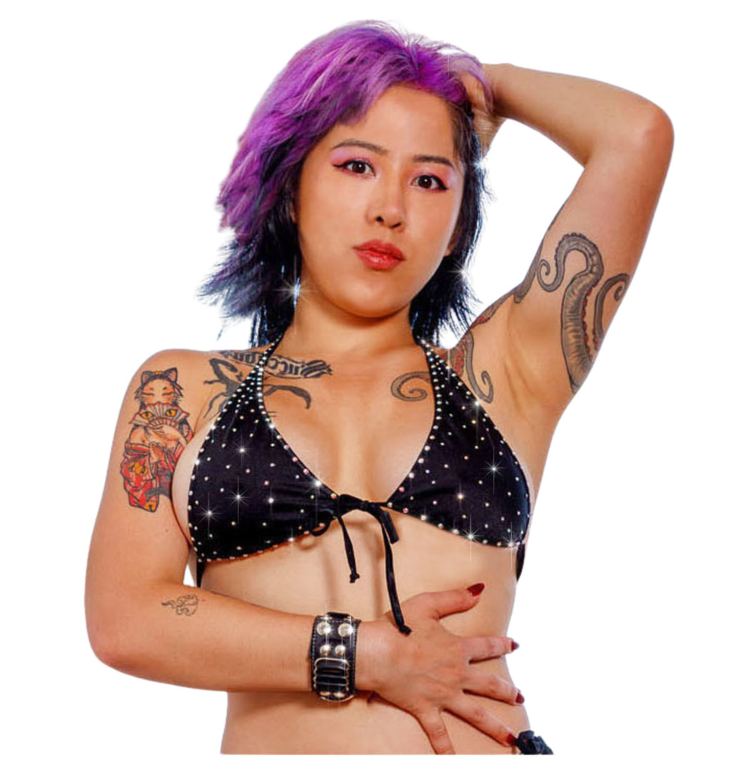 A model with purple hair is modeling a micro black halter top  covered in rhinestones with a plain white background.