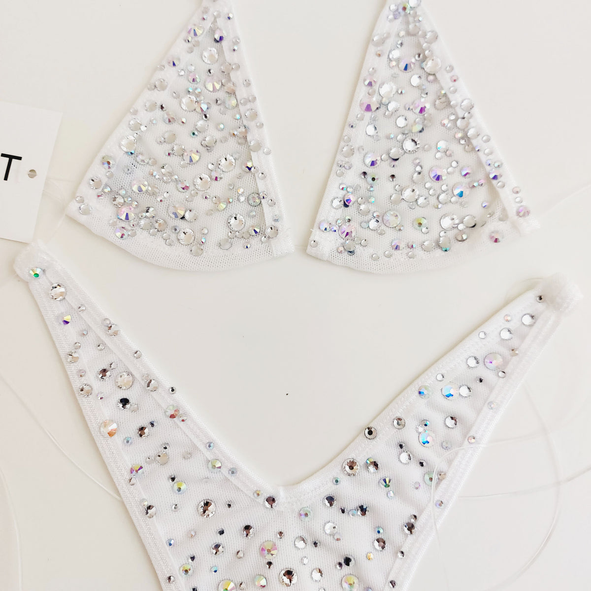 White bikini-style lingerie pieces covered with iridescent rhinestones, arranged on a light neutral background.