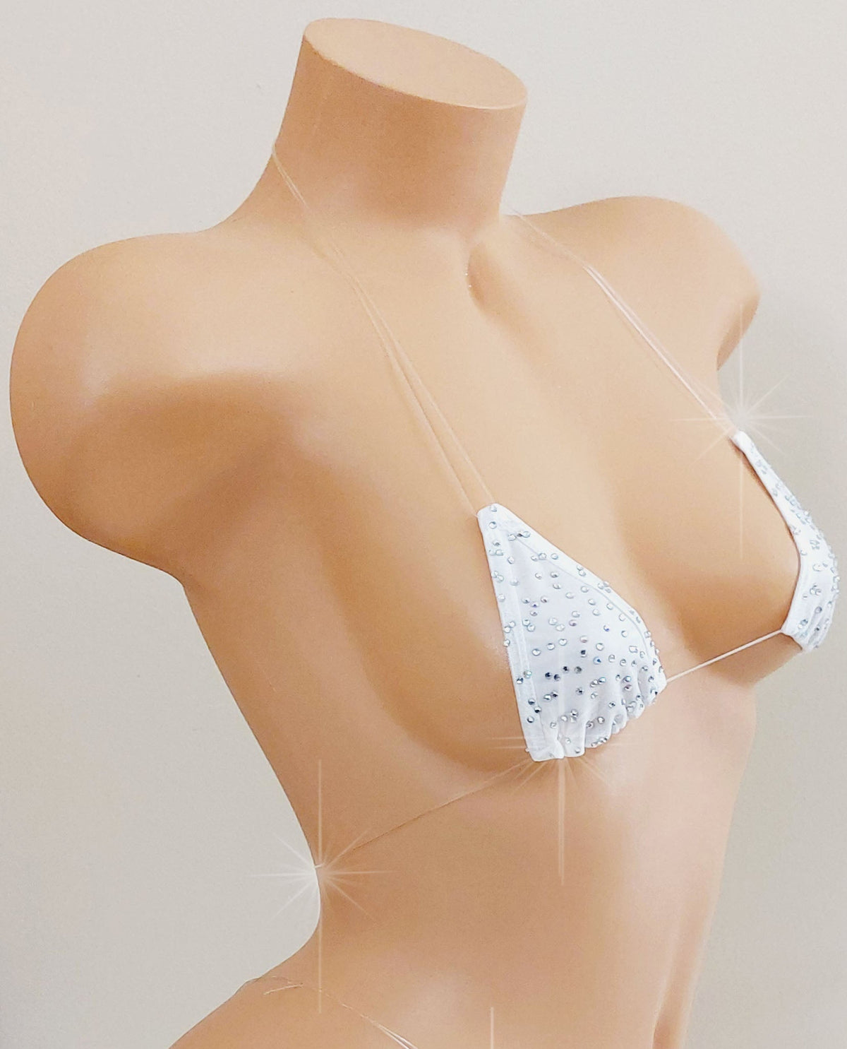 Side view of a White skimpy bikini with rhinestones and invisible clear elastic straps on a mannequin torso against a blank background.