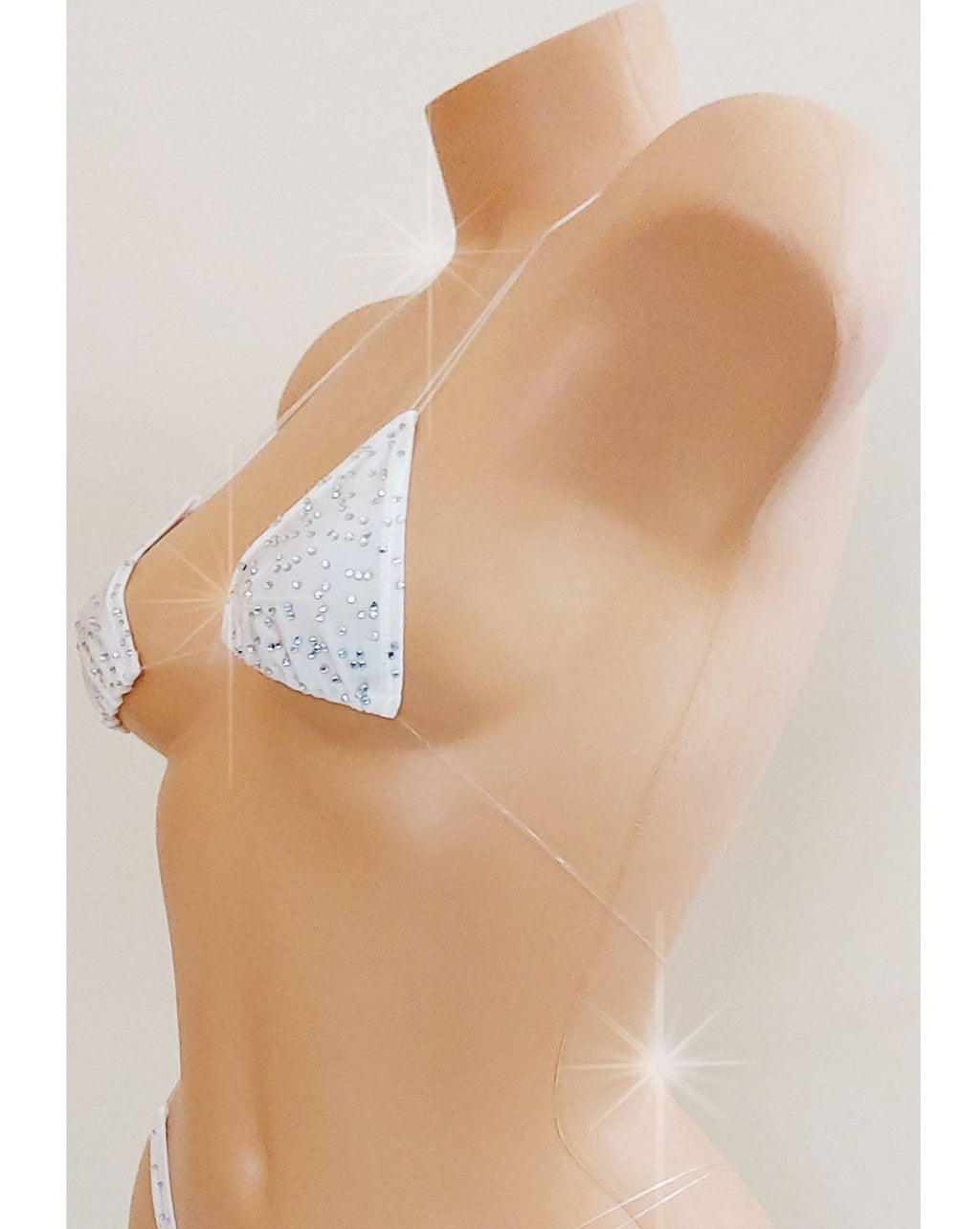 Side view of a White skimpy bikini with rhinestones and invisible clear elastic straps on a mannequin torso against a blank background.