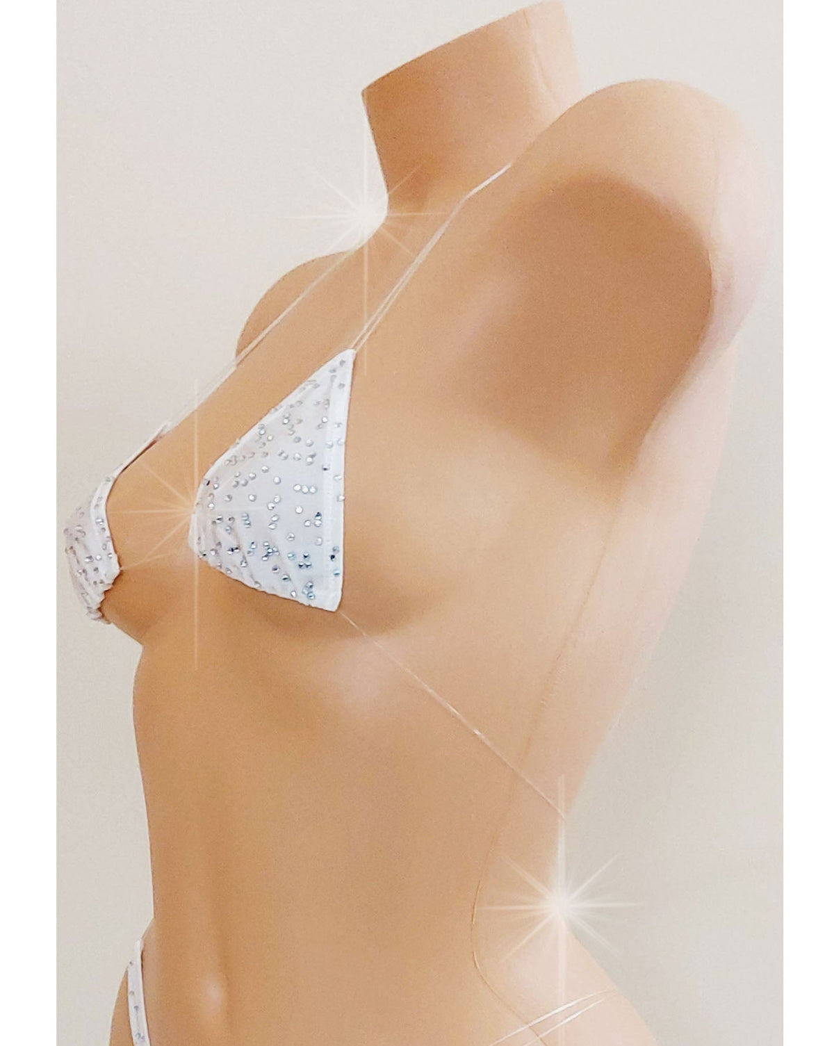 Side view of a White skimpy bikini with rhinestones and invisible clear elastic straps on a mannequin torso against a blank background.
