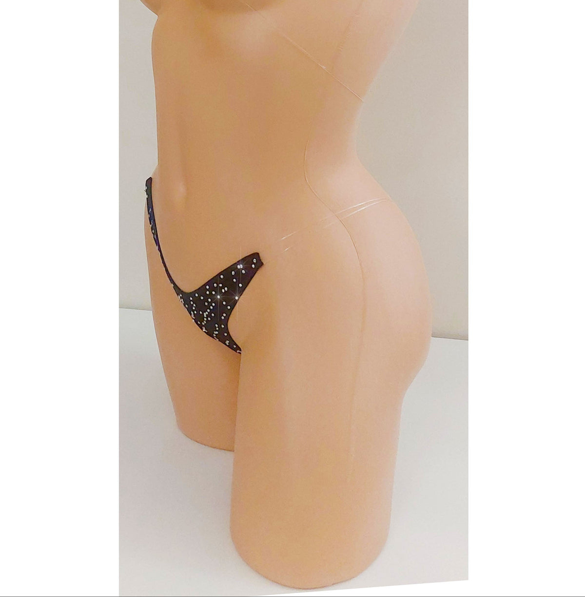 Black invisible strap micro bikini g-string thong covered in rhinestones on a torso mannequin on a white background.
