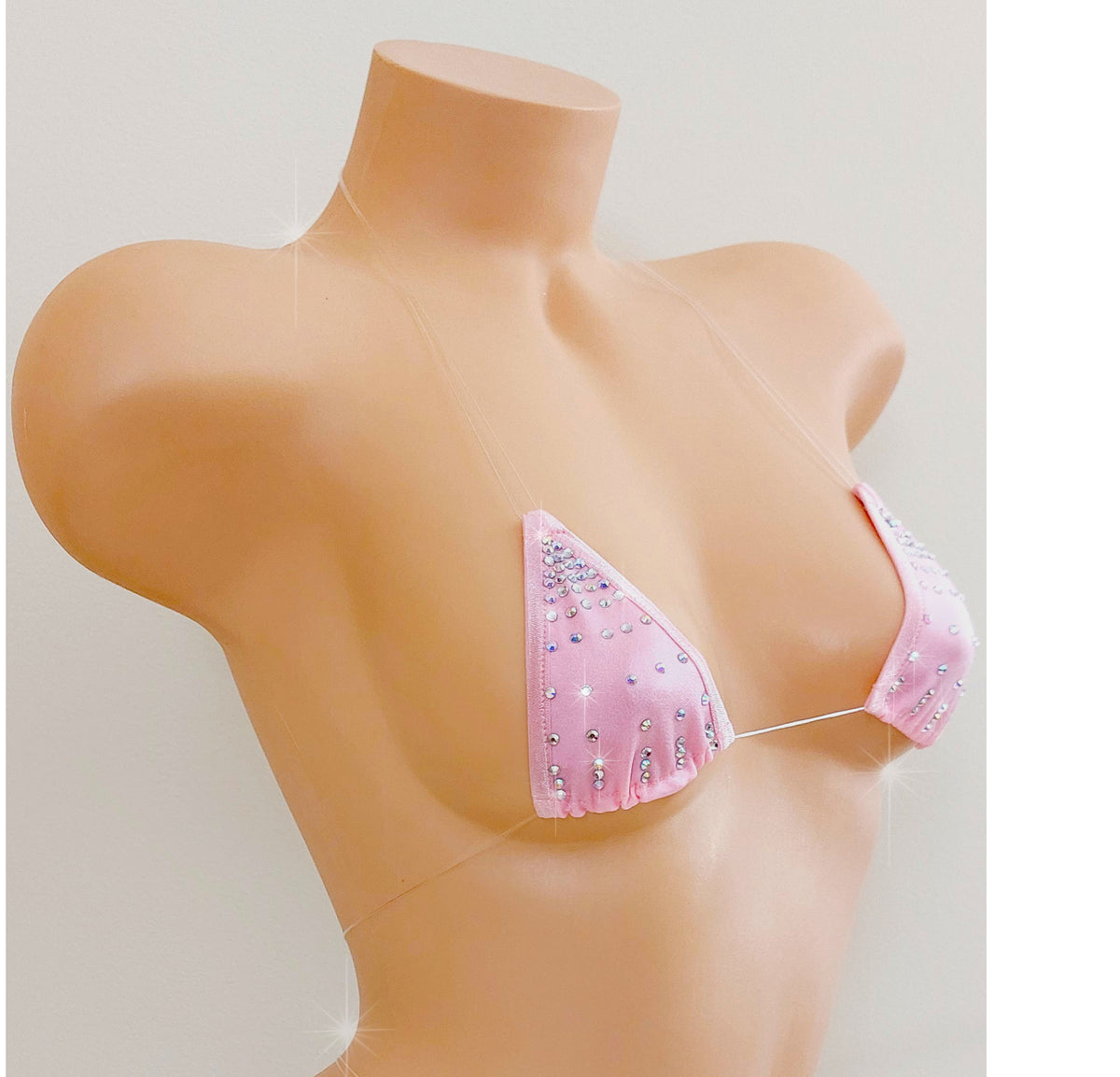 A baby pink rhinestone triangle bikini top with clear straps that appear invisible on a female plastic beige torso against a plain background.