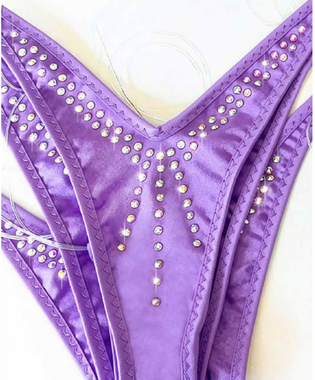 A close-up of a purple bikini bottom with rhinestone embellishments, showing the V-shape and side panels on a light background.