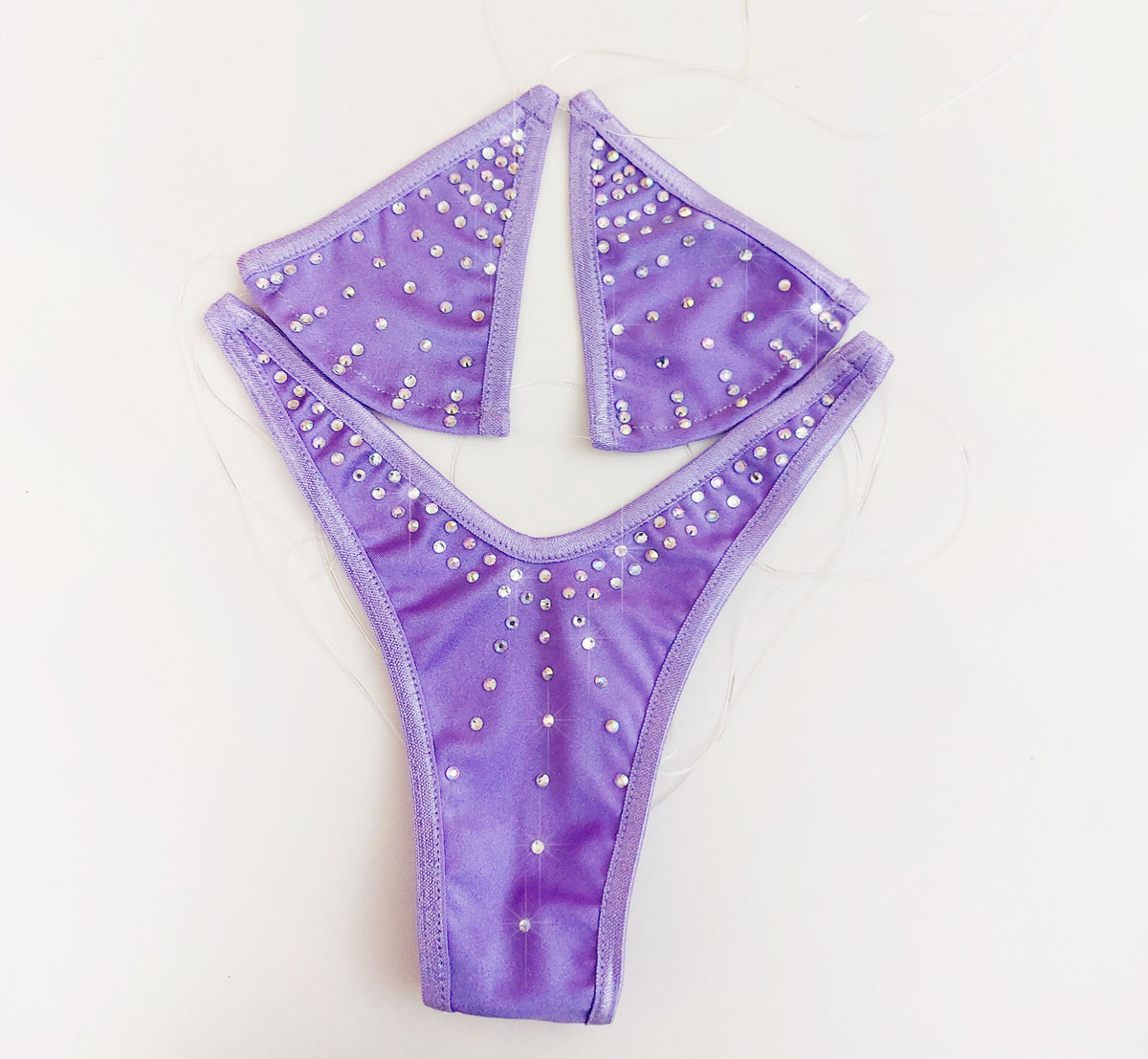 Product shot of a purple lavender rhinestone design triangle bikini top with clear straps laid flat on a plain background.