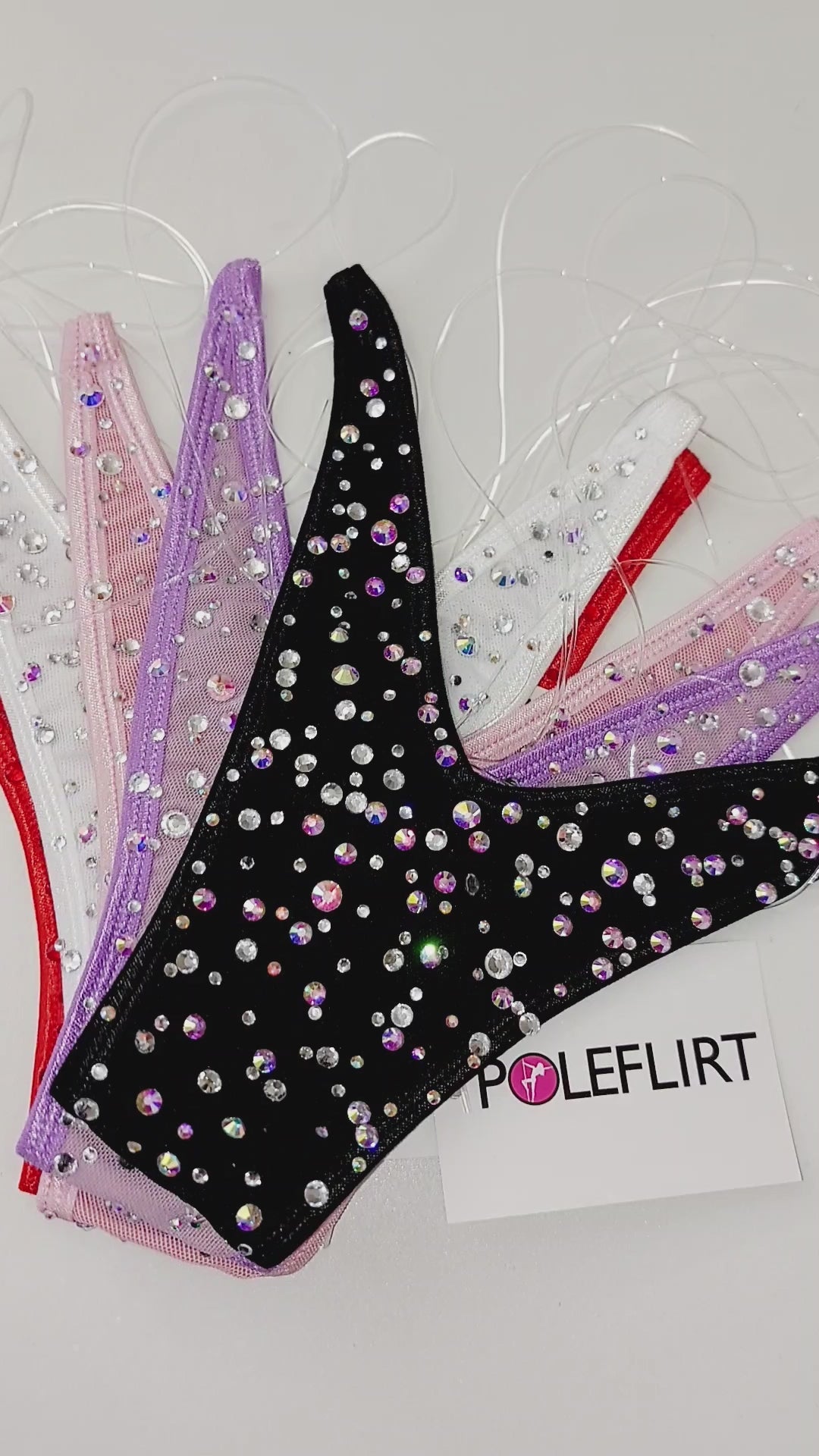 Video with brand name PoleFlirt displayed above5 different colored micro bikini thong bottoms, covered in small bedazzled rhinestones laid flat against a white background.